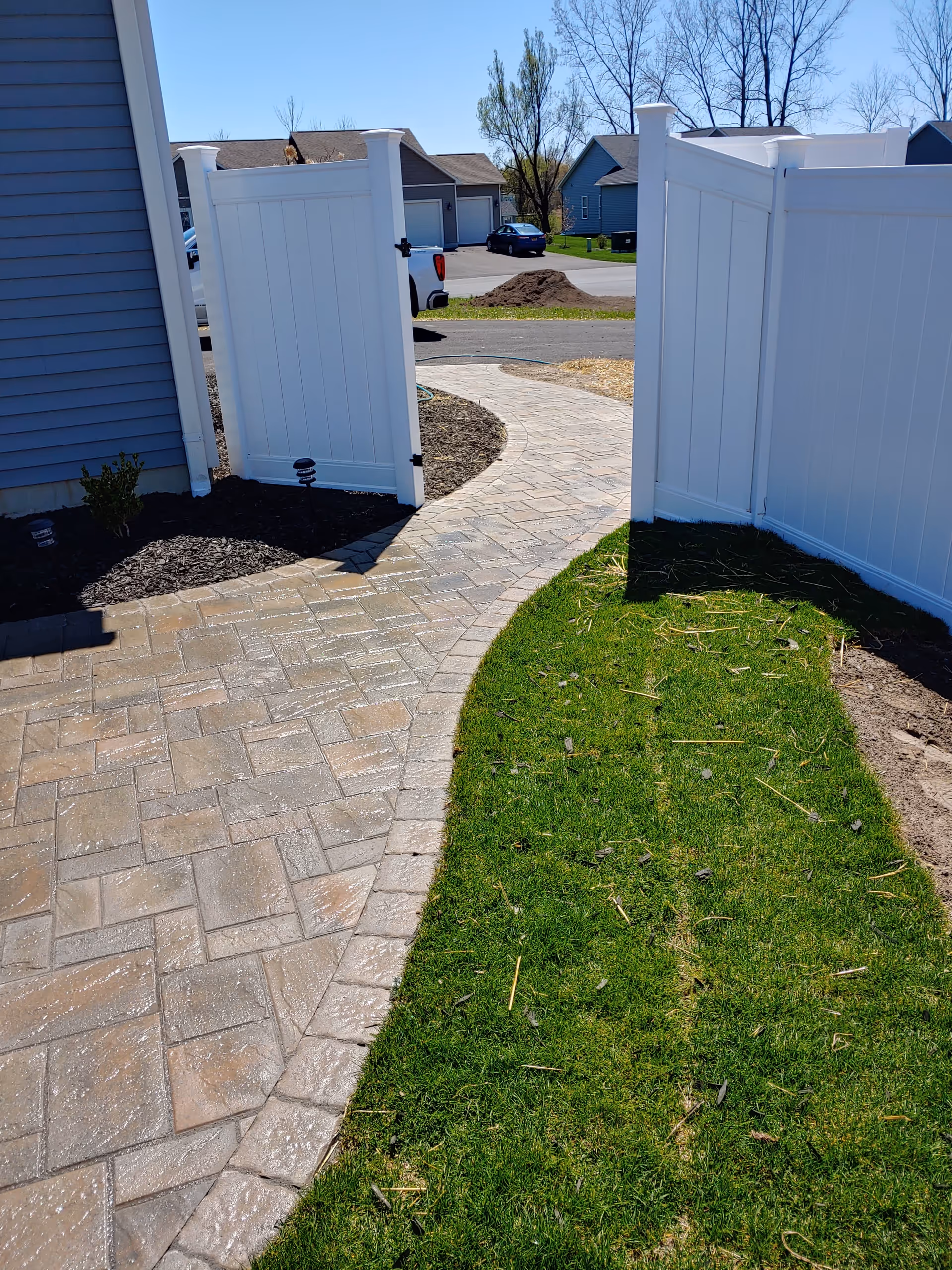 Open white vinyl gates frame a curved brick walkway to a residential retirement community.