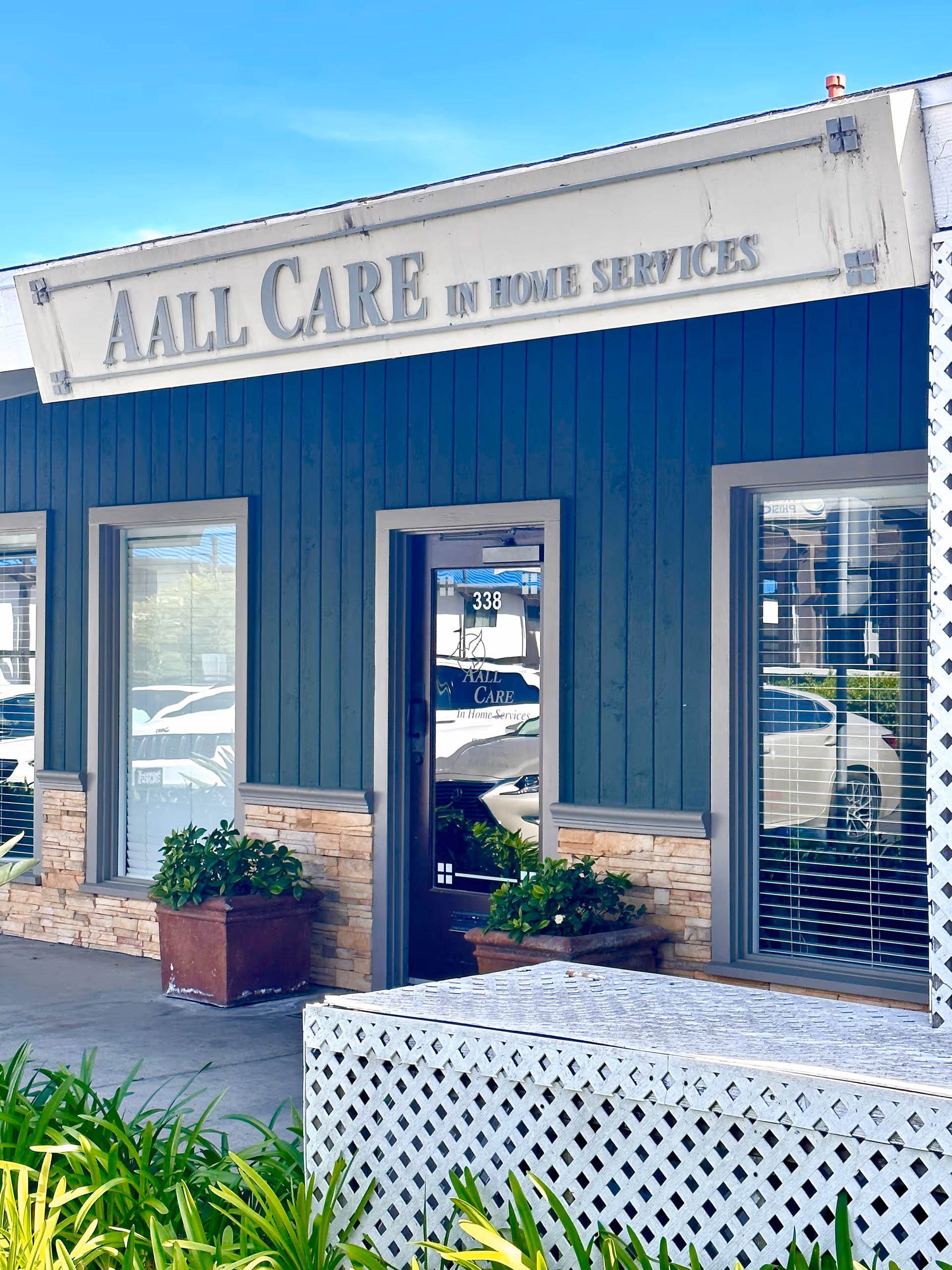 Blue storefront with AALL CARE sign, windows, and potted plants at entrance.
