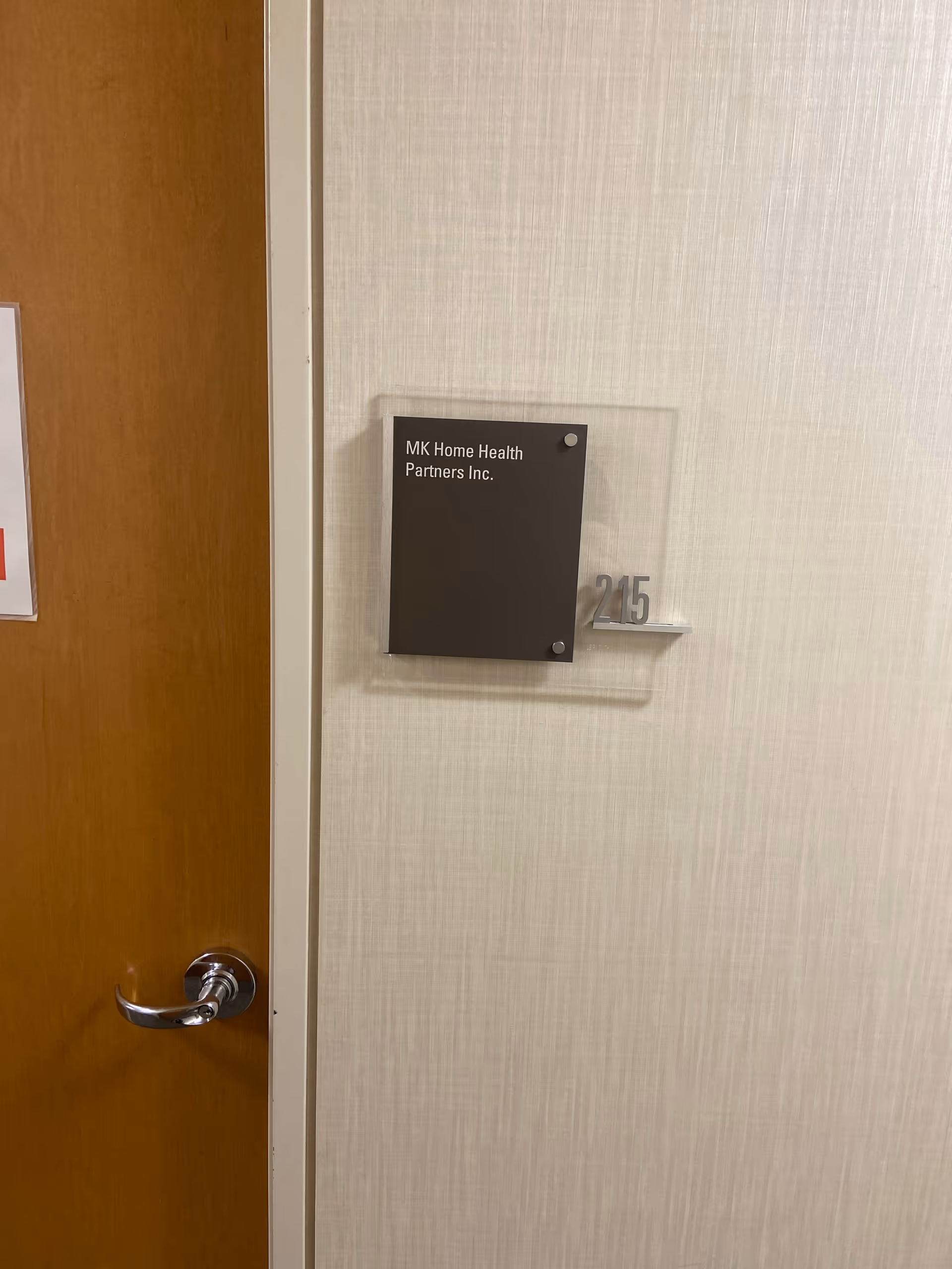 Interior hallway with wooden door and wall plaque reading MK Home Health Partners, Inc., room 215.