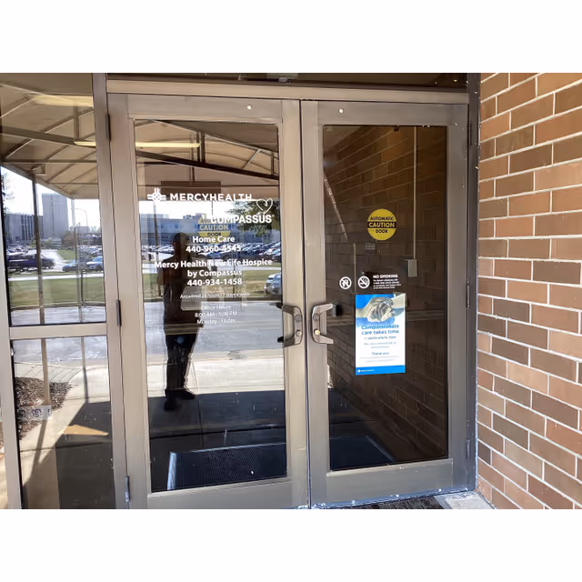 Glass doors display Mercy Health New Life Hospice by Compassus signage at the entrance.