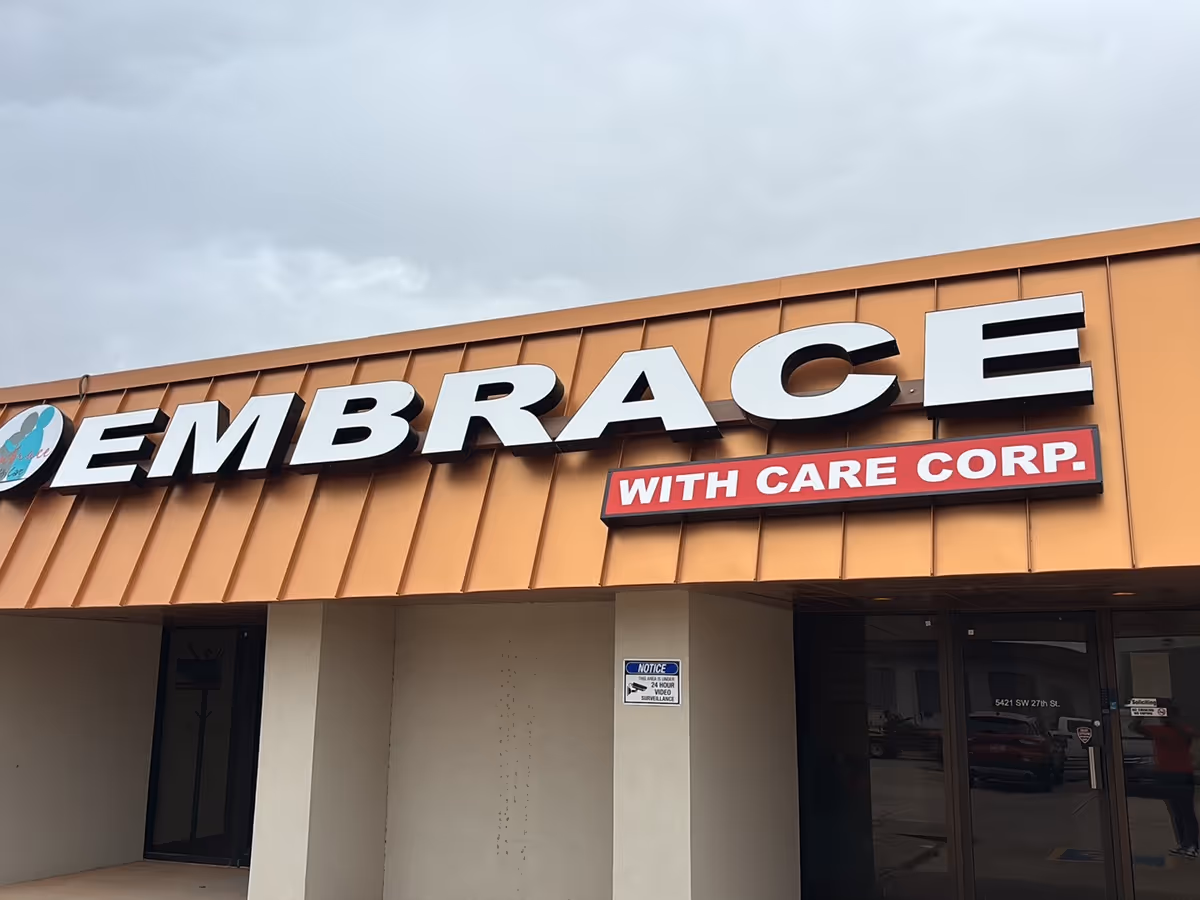 Orange storefront exterior with a large EMBRACE sign and 'WITH CARE CORP' banner.