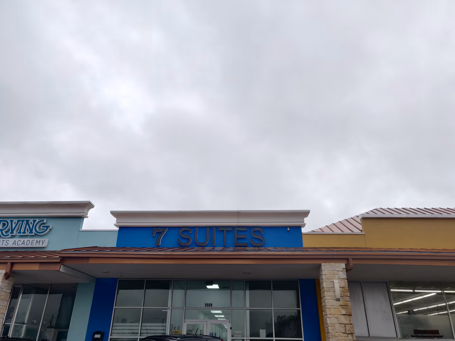 Exterior view of a building with blue 7 SUITES sign against cloudy sky.
