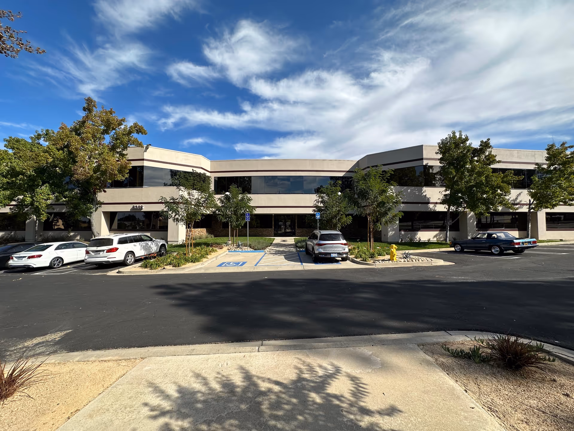 Two-story beige building with parked cars in front and a blue sky.
