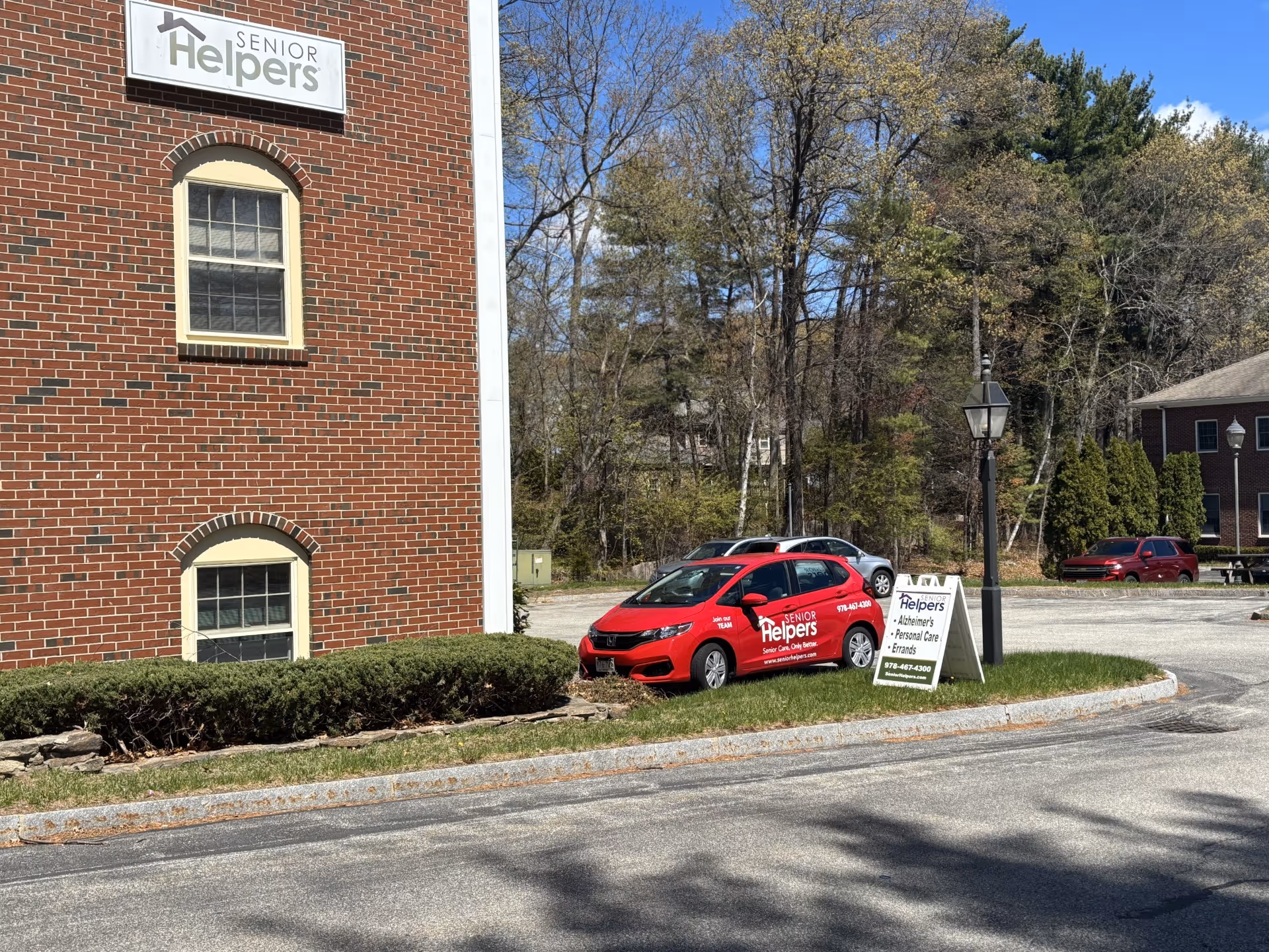 Brick building front with Senior Helpers sign, red branded car, and a small grassy curb area