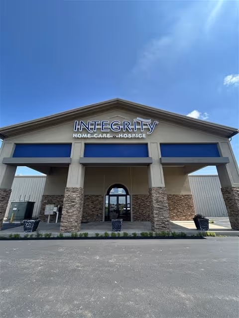 Front exterior of Integrity Home Care Hospice building with stone columns and blue awnings.