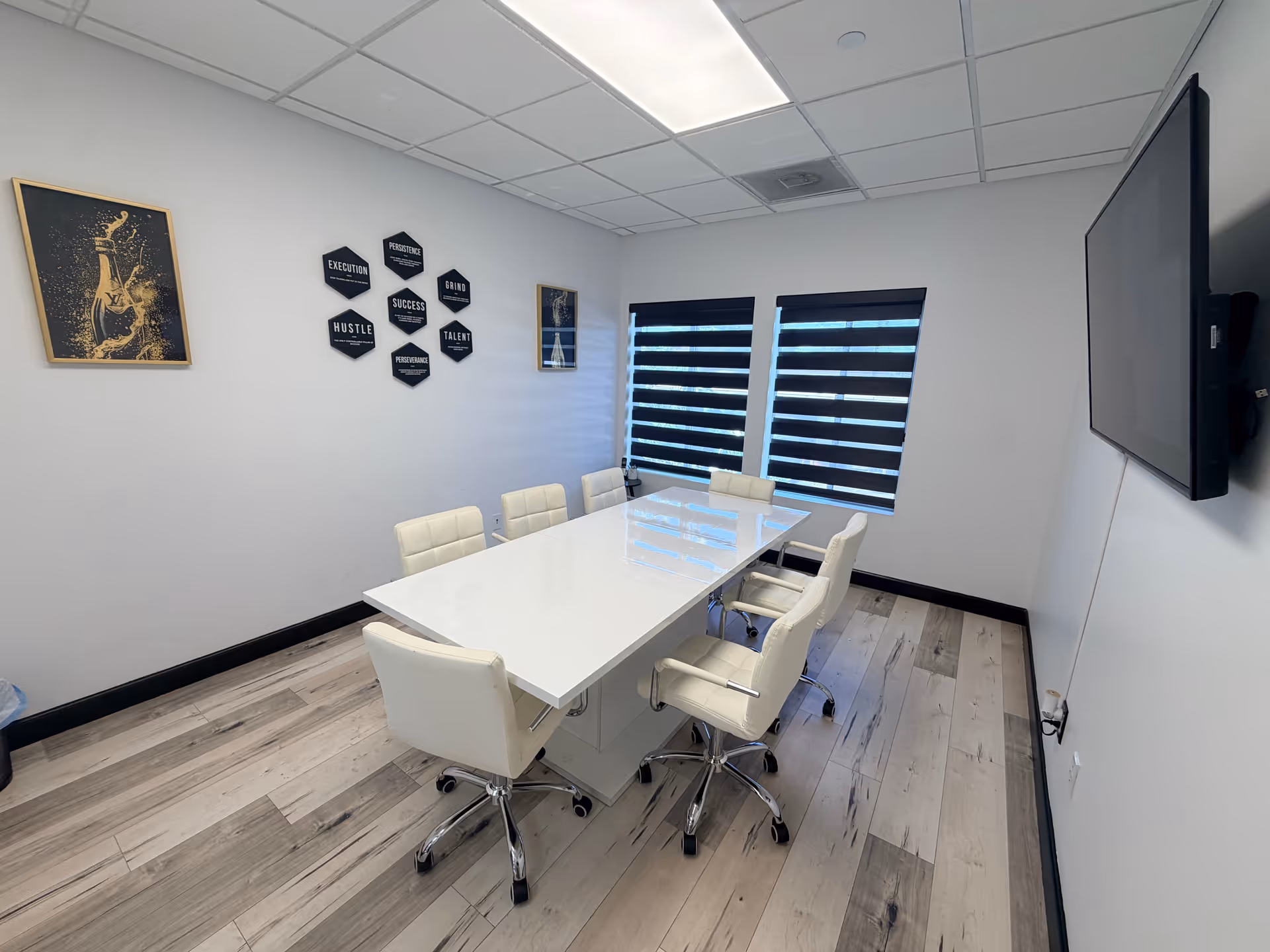 A modern conference room with a white table, white chairs, wall art, and a mounted TV.