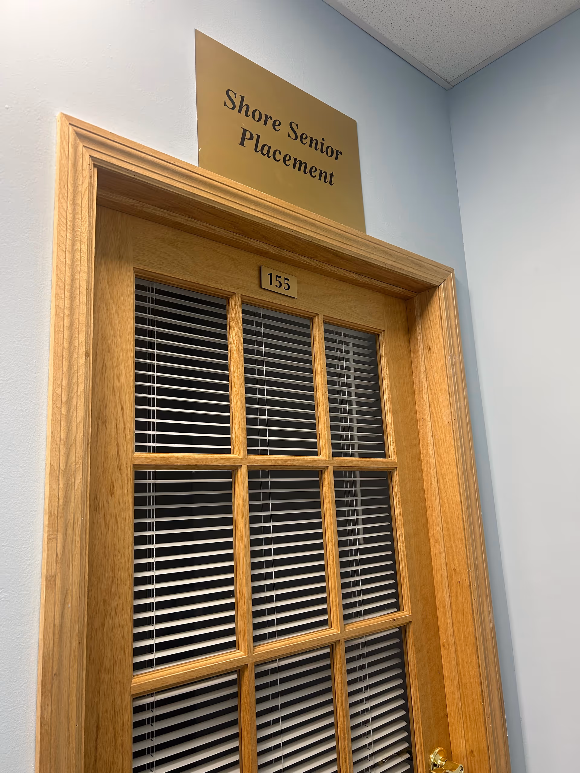 Interior wood-framed door labeled Shore Senior Placement with blinds behind glass.