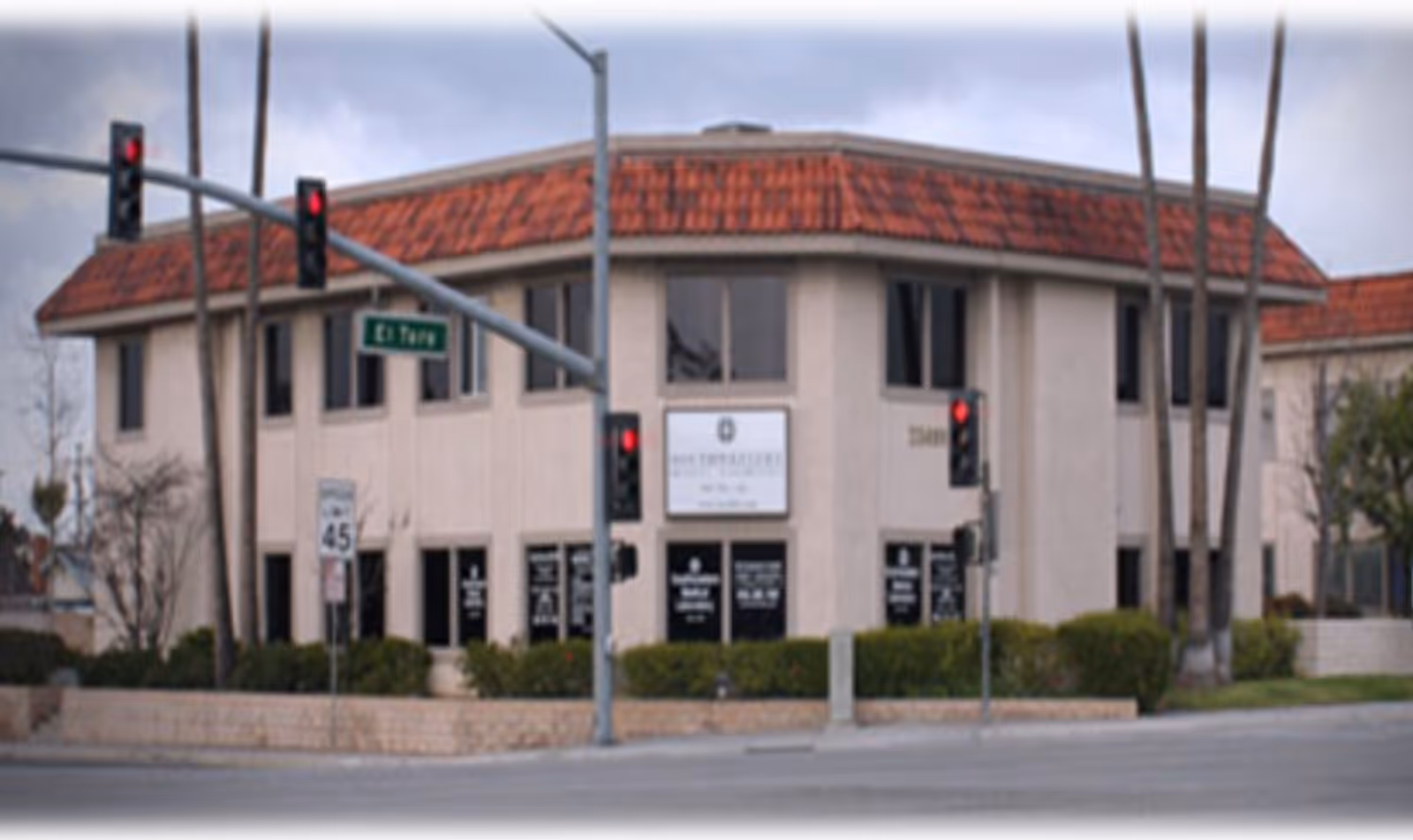 Exterior of a beige, two-story building with a red-tiled roof at a street intersection.