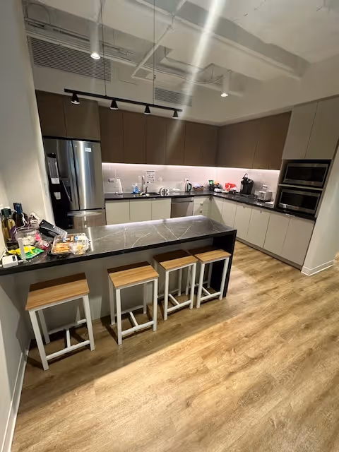 Modern kitchen with island, stools, stainless appliances, and overhead lighting in a senior living facility.