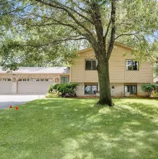 Two-story beige senior living facility with a large tree in the front yard.