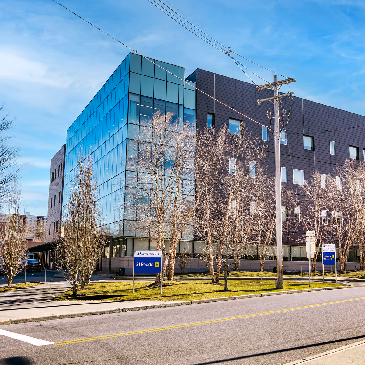 Modern glass-front medical building along a street with bare trees.