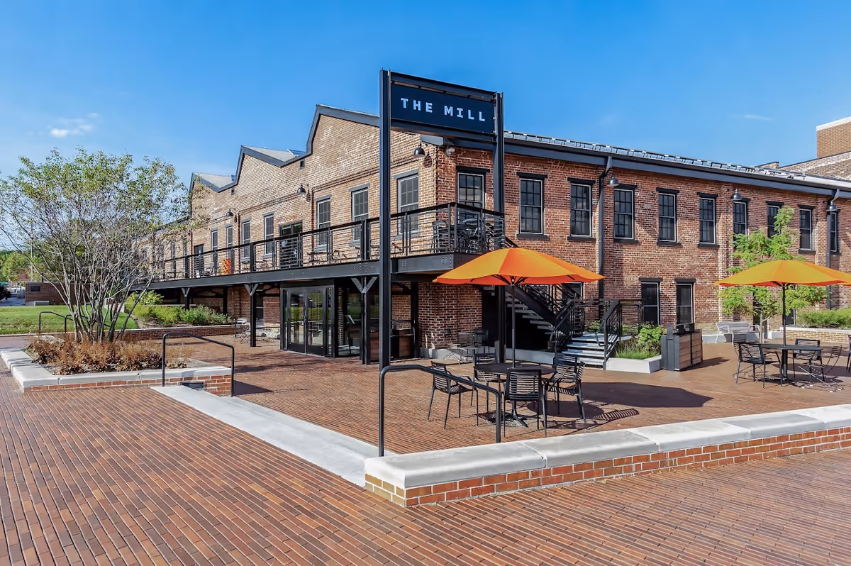 Outdoor brick courtyard with black tables and orange umbrellas in front of a two-story brick building.