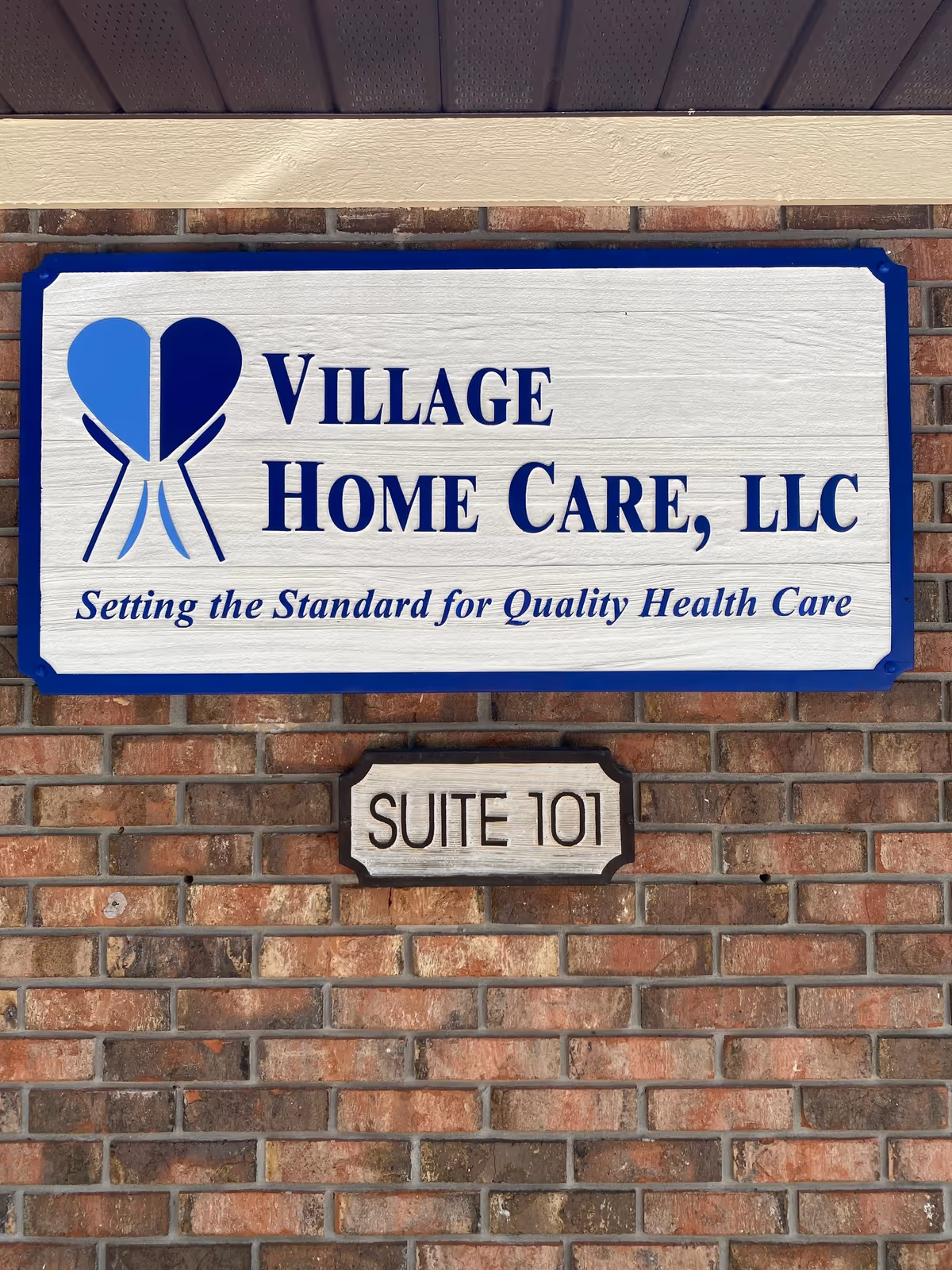 Brick exterior wall with Village Home Care, LLC sign and Suite 101 plaque.