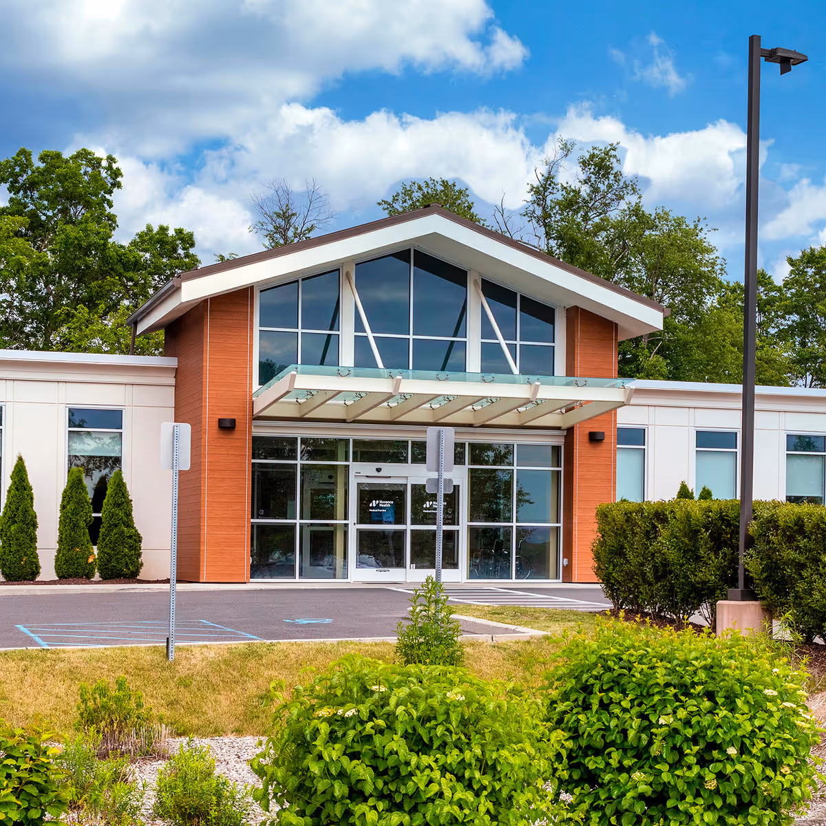Modern building entrance with glass doors, brick accents, and manicured shrubs.