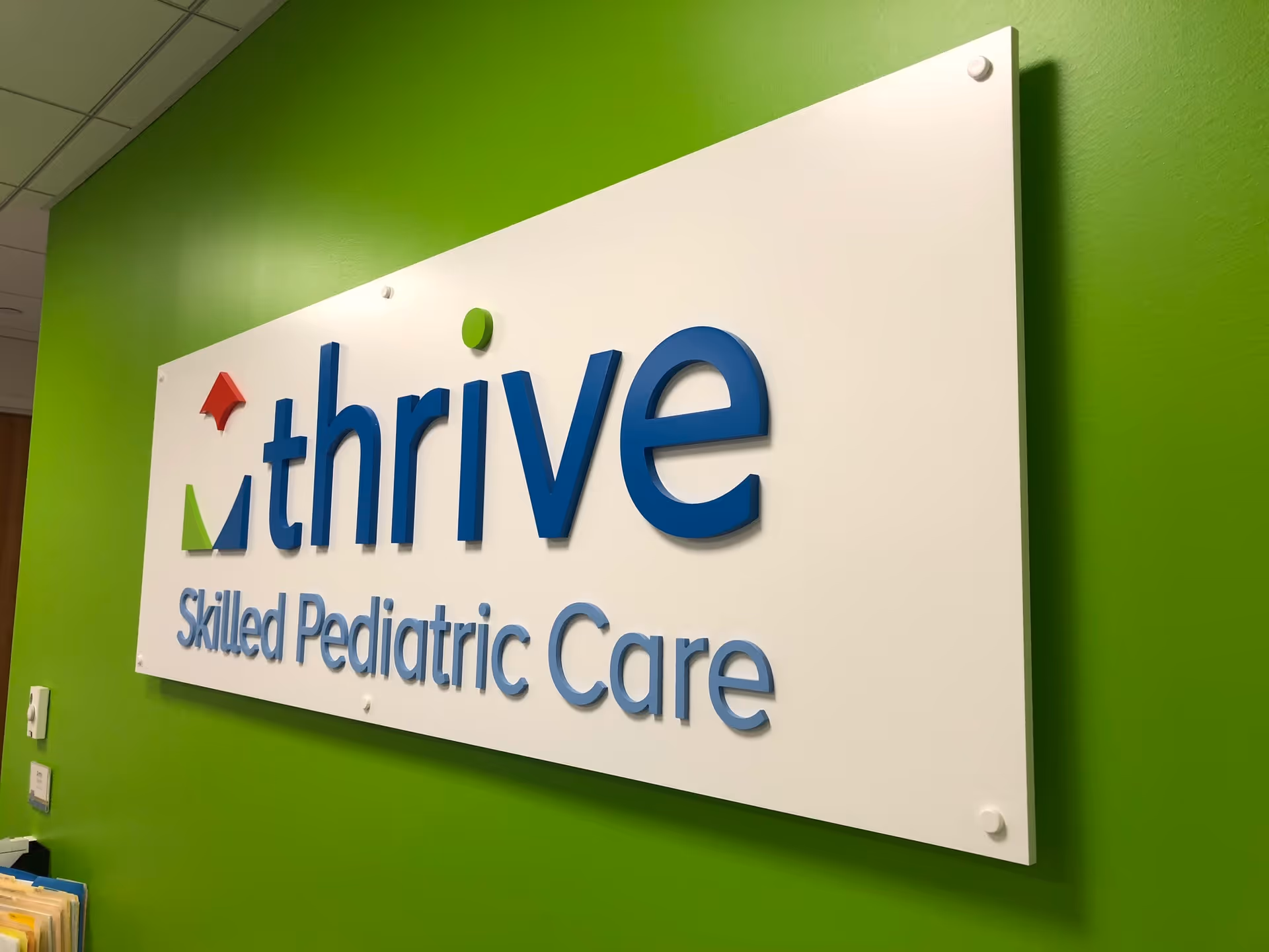 Bright green interior wall with a large Thrive Pediatric Care sign plaque.