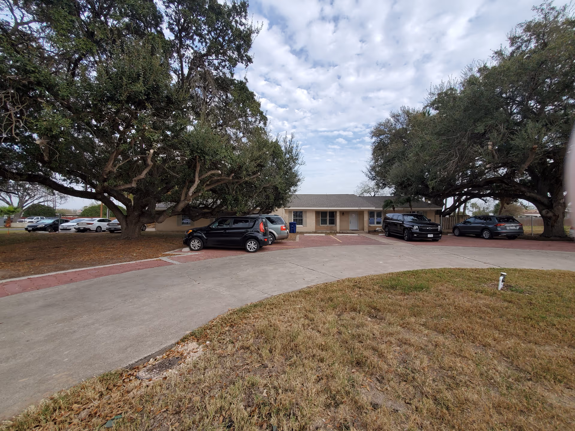 Pan De Vida Healthcare building exterior with parked cars and large trees.