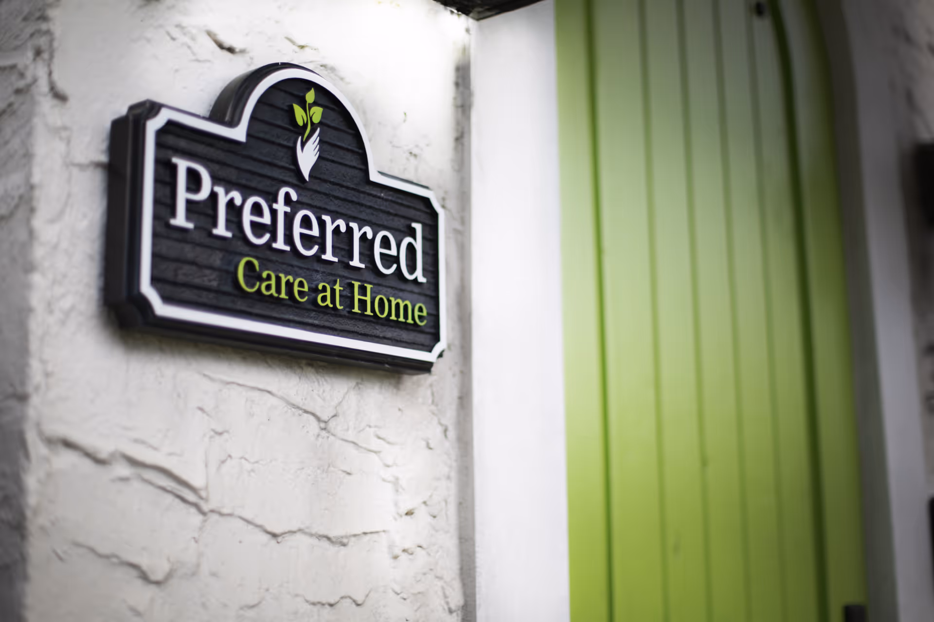 Sign reads 'Preferred Care at Home' on a textured wall beside a green door.