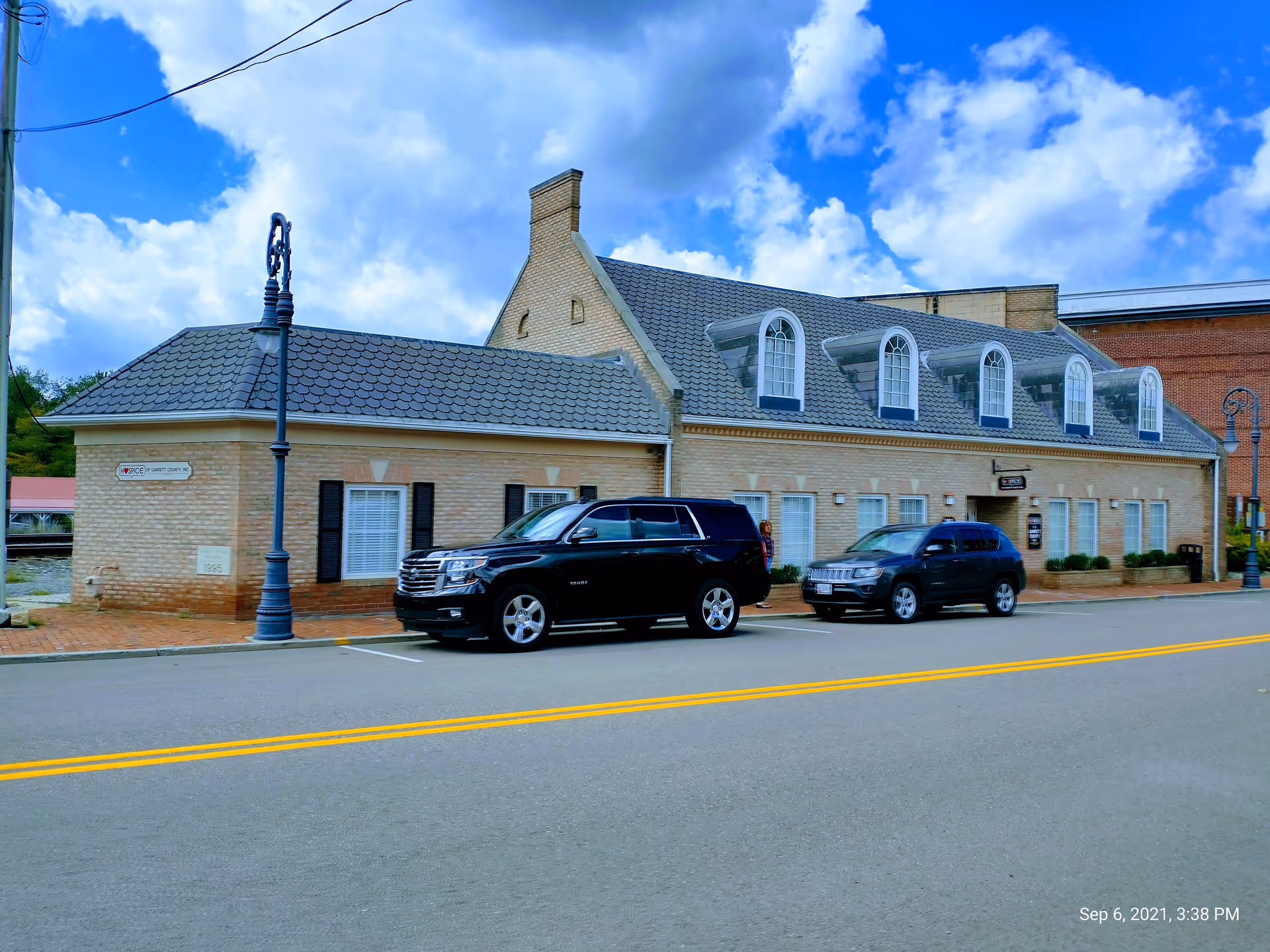 Brick facility front with dormer windows and parked cars along a street.