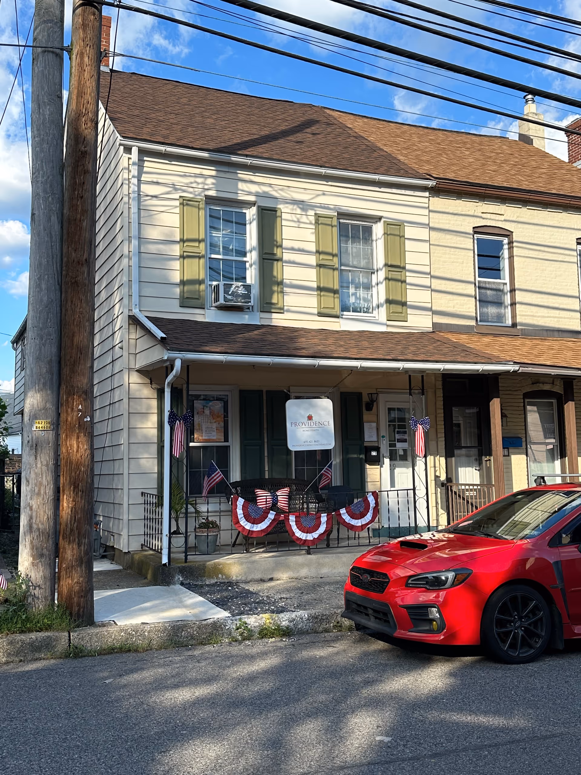 Two-story building with front porch, patriotic bunting and a Providence sign; red car parked roadside.