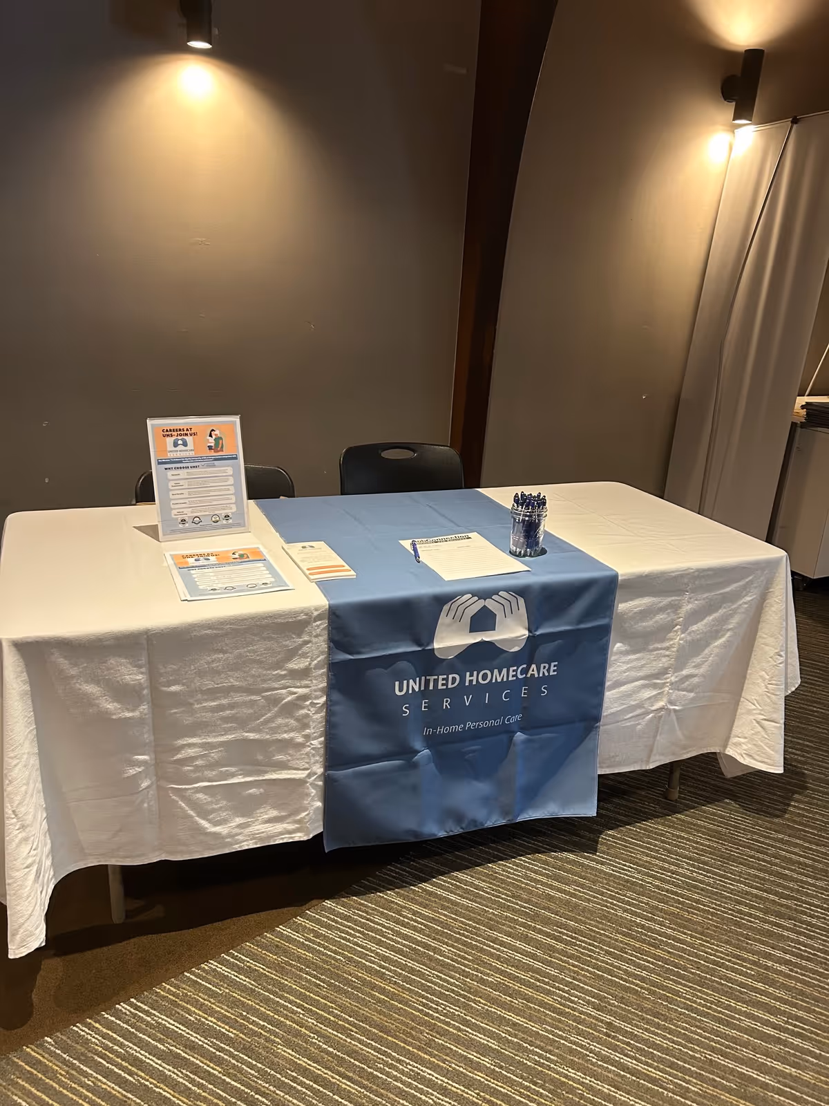 Indoor information table with a blue United Homecare Services banner and pamphlets.
