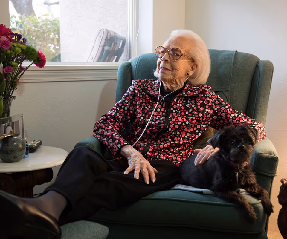 Elderly woman relaxing in a green armchair with a small black dog.
